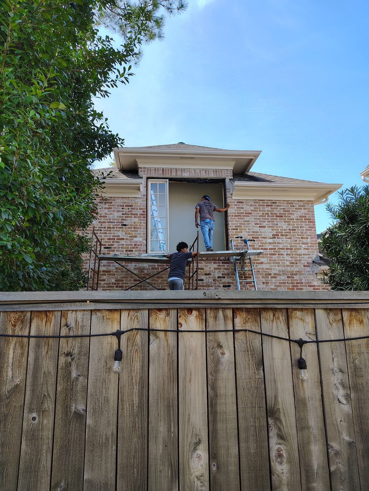 Two workers installing a large window on a brick two-story home